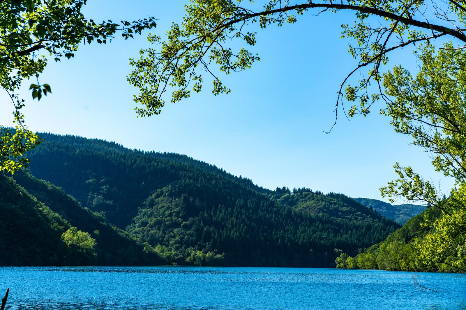 Le lac aux eaux bleues sous les feuillages, collines boisées
